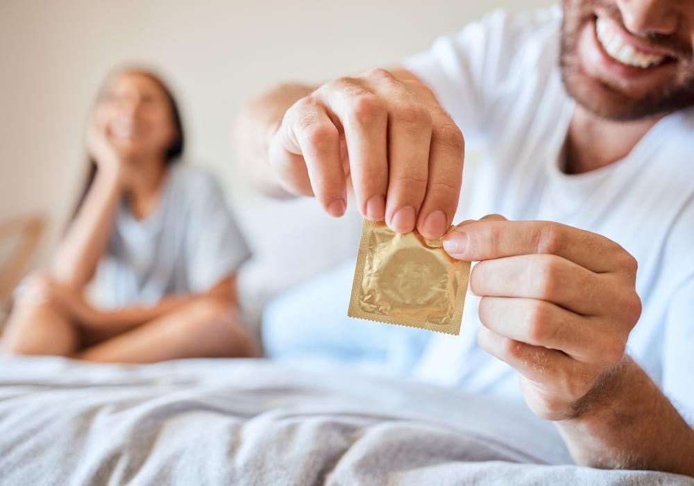 FAQ_Kondomgroessen_richtige_passform_vom_kondom_finden_paar_liegt_im_bett_und_oeffnet_Kondompackung.jpg