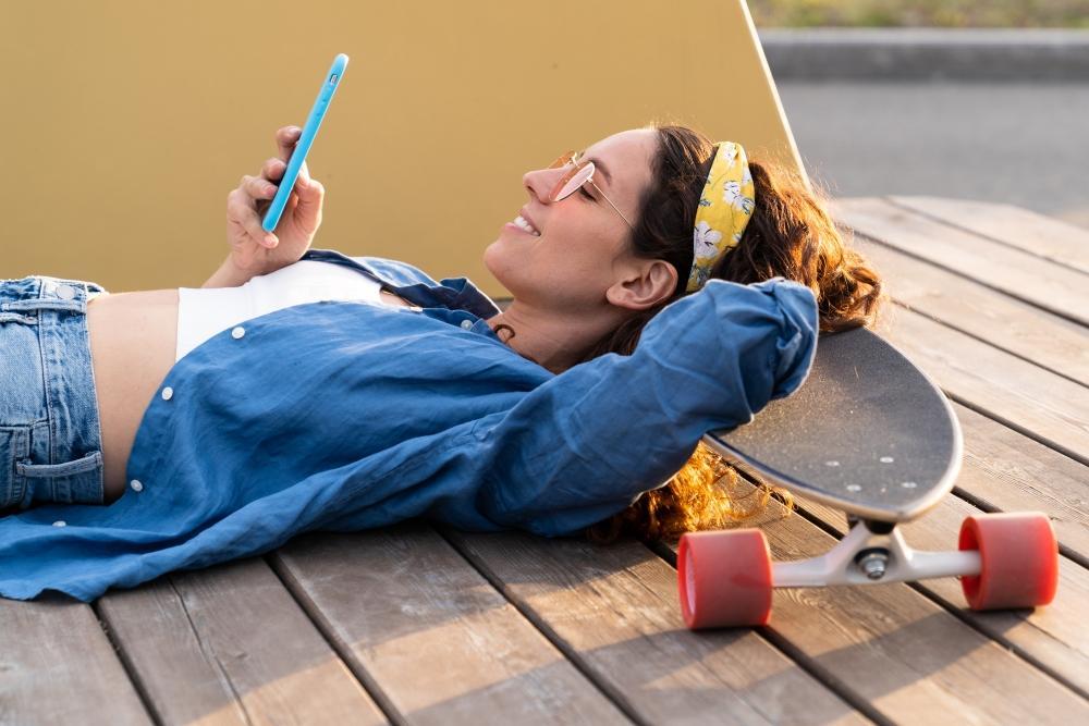 anzeichen_dass_du_poppen_solltest_mehr_lust_ist_kein_problem_schlechte_kompromisse_sind_eins_Frau_liegt_auf_dem_boden_guckt_gluecklich_auf_ihr_handy_