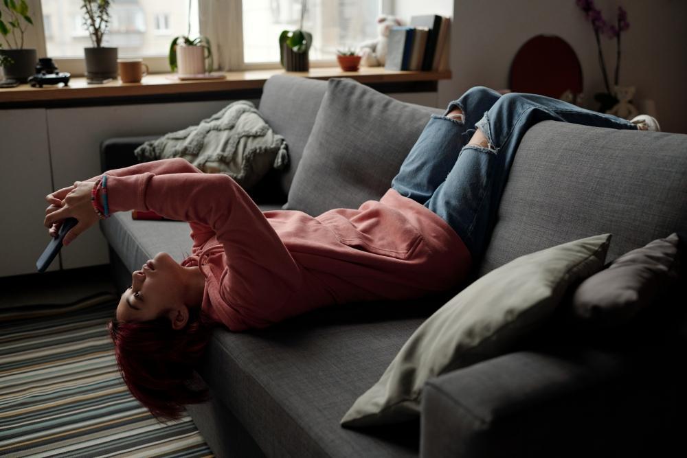 sieben_signale_dass_sie_dringend-mal_wieder_poppen_muessen_Frau_auf_dem_sofa_gelangweilt_schaut_auf_ihr_handy_